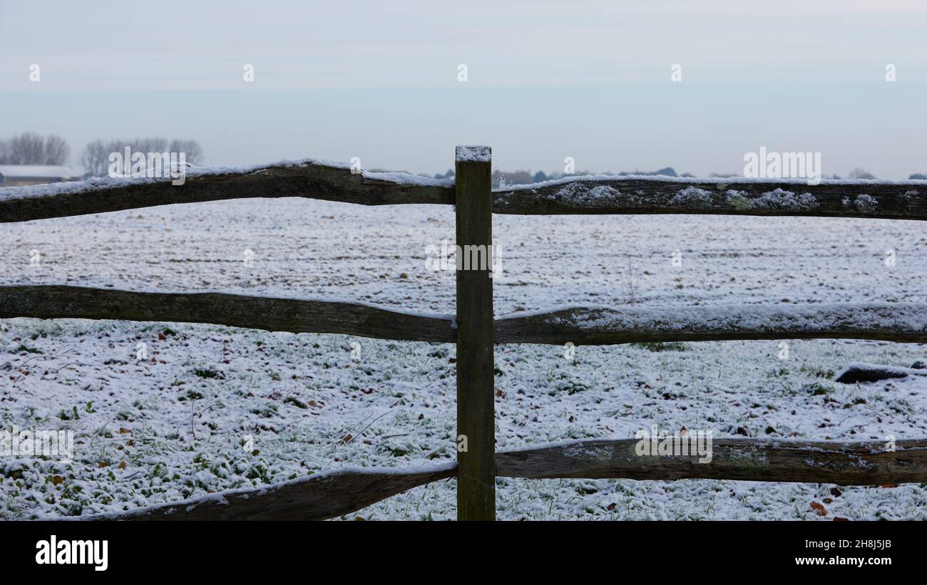 Pfosten- und Schienenzäune am Rand des Ackerlandes, das von einem Stauben von Schnee bedeckt ist. Stockfoto
