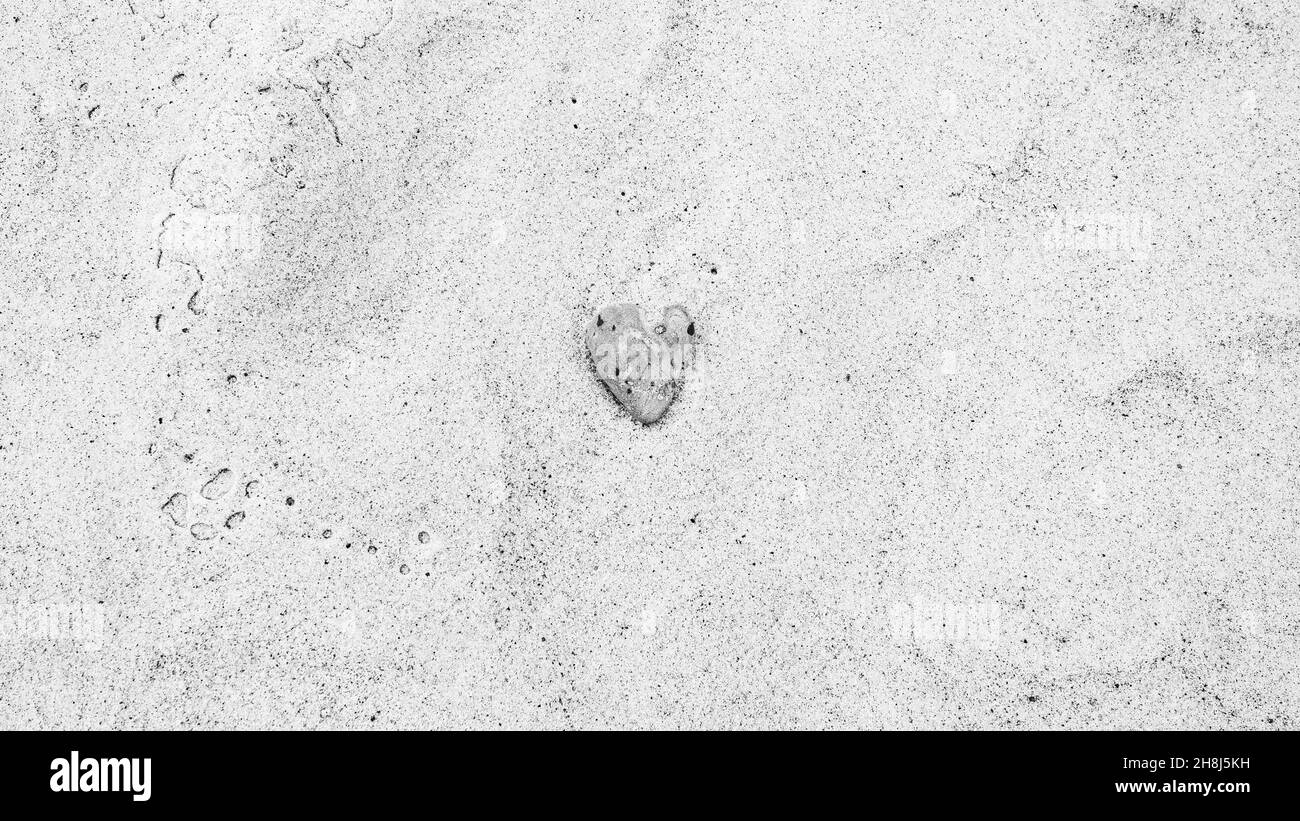 Herzförmiger grauer Meeresfelsen am Sandstrand, Schwarz-Weiß-Foto Stockfoto