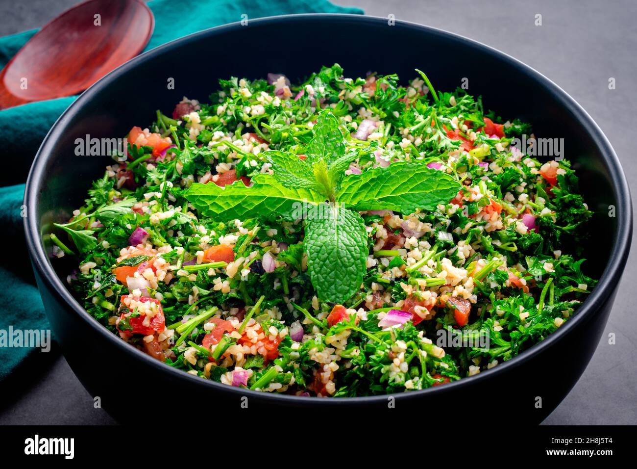 Authentisches libanesisches Tabbouleh garniert mit Minzblättern: Eine große Servierschüssel mit Petersiliensalat mit Bulgur-Weizen, Tomaten und Zwiebeln Stockfoto