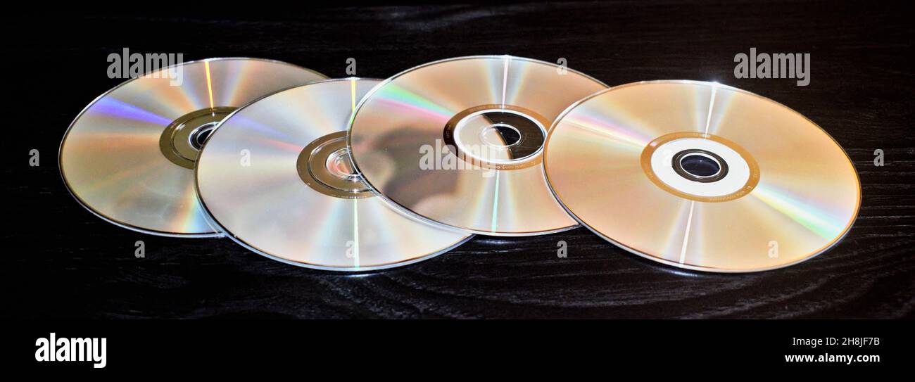 Vier leere CDs verteilen sich auf einem schwarzen Tisch mit selektivem Fokus und sind isoliert. Stockfoto
