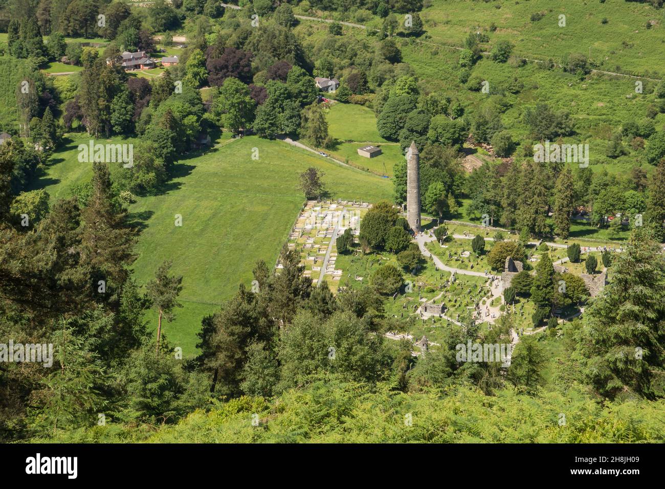 Blick von oben auf die frühmittelalterliche Klostersiedlung mit dem Round Tower, eingebettet in ein waldreiches Gletschertal im Glendalough National Park. Stockfoto