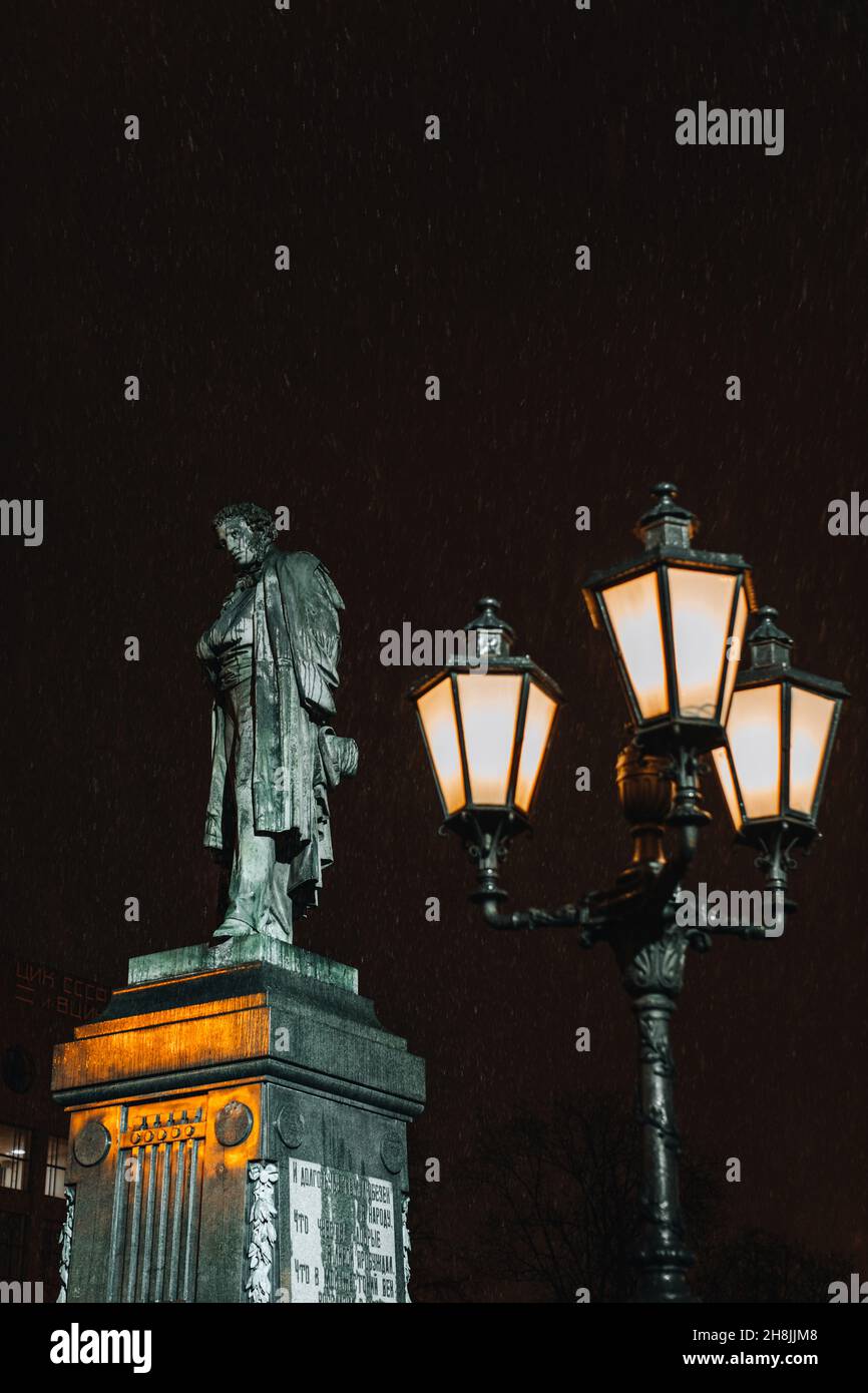 Denkmal des russischen berühmten Dichters Alexander Puschkin auf dem Puschkin-Platz, Moskau, Russland. Brennende Laterne im Abendlicht und fallender Schnee Stockfoto