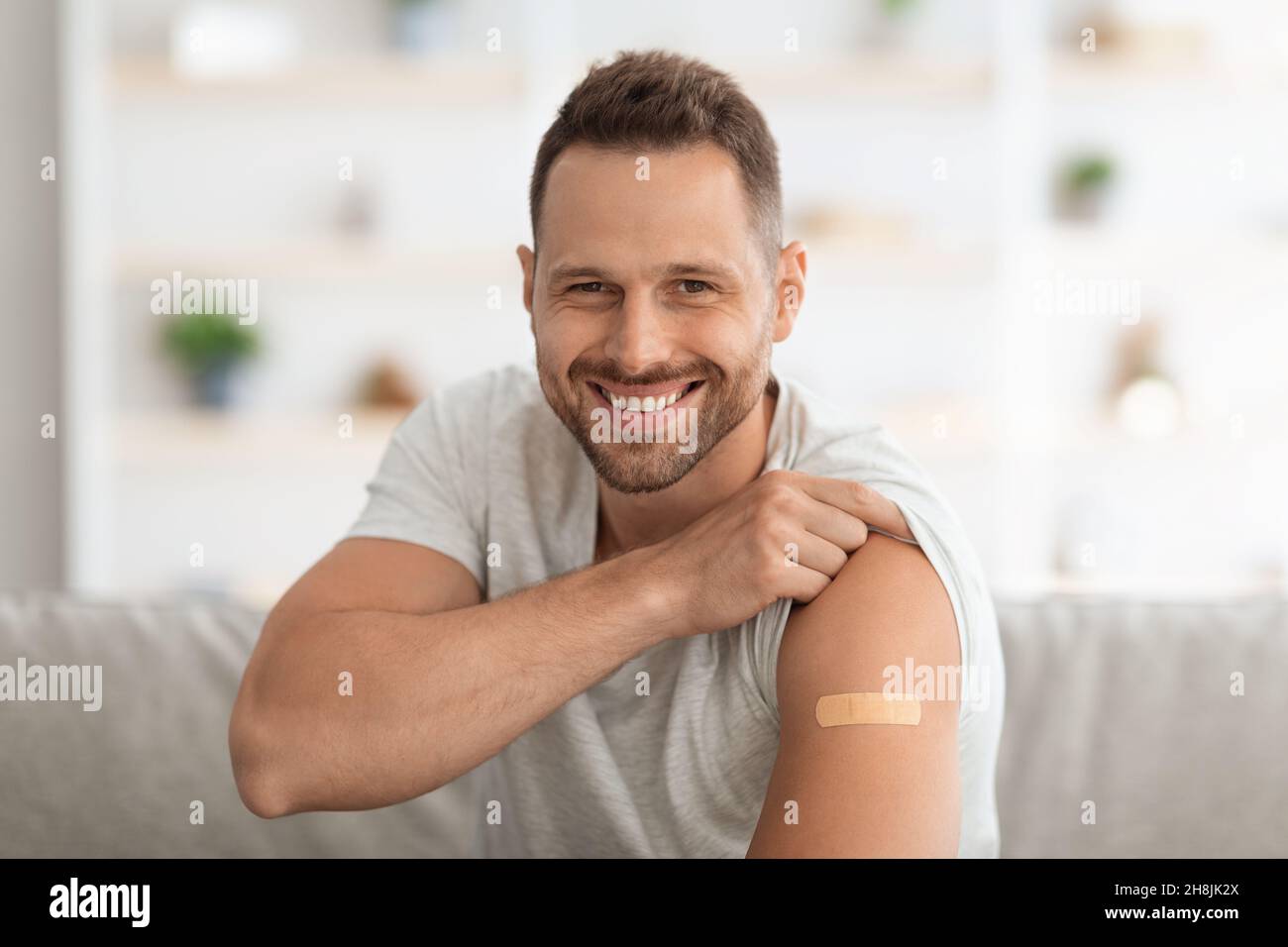 Positiver junger geimpfter Mann, der nach der Impfstoffinjektion seine Schulter mit medizinischem Gips zeigte und lächelte vor der Kamera Stockfoto
