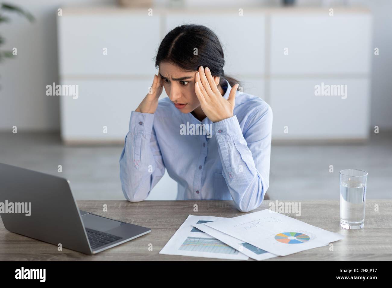 Schockiert verärgert müde tausendjährige hindu-Managerin drückt die Hände an die Tempel und schaut auf den Laptop Stockfoto