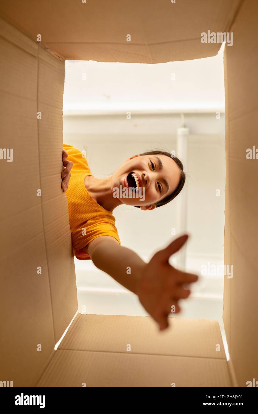 Bottom View der emotionalen koreanischen Frau, die online bestellt wurde und ihr Kartonpaket zu Hause auspackte Stockfoto
