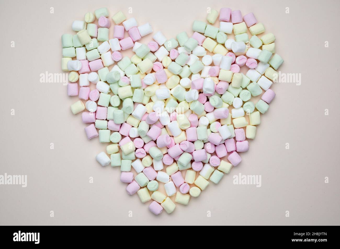 Mini-Marschmallows liegen in Herzform auf pastellfarbenem Hintergrund Stockfoto