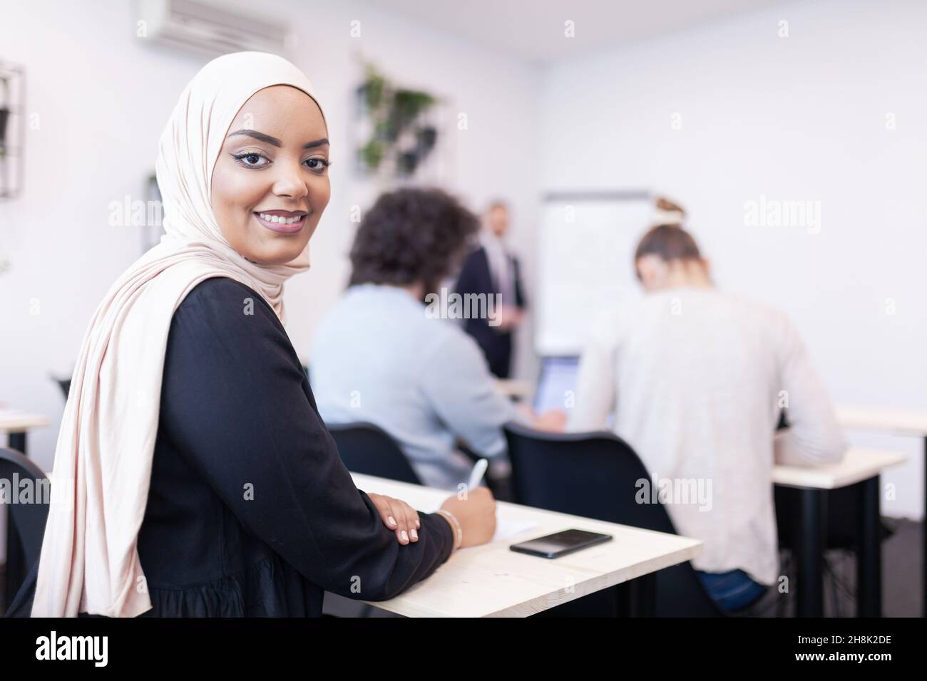 Multiethnische Studenten hören einem Dozenten in einem Klassenzimmer zu. Intelligente junge afroamerikanische Frau lächelt und posiert für die Kamera. Stockfoto