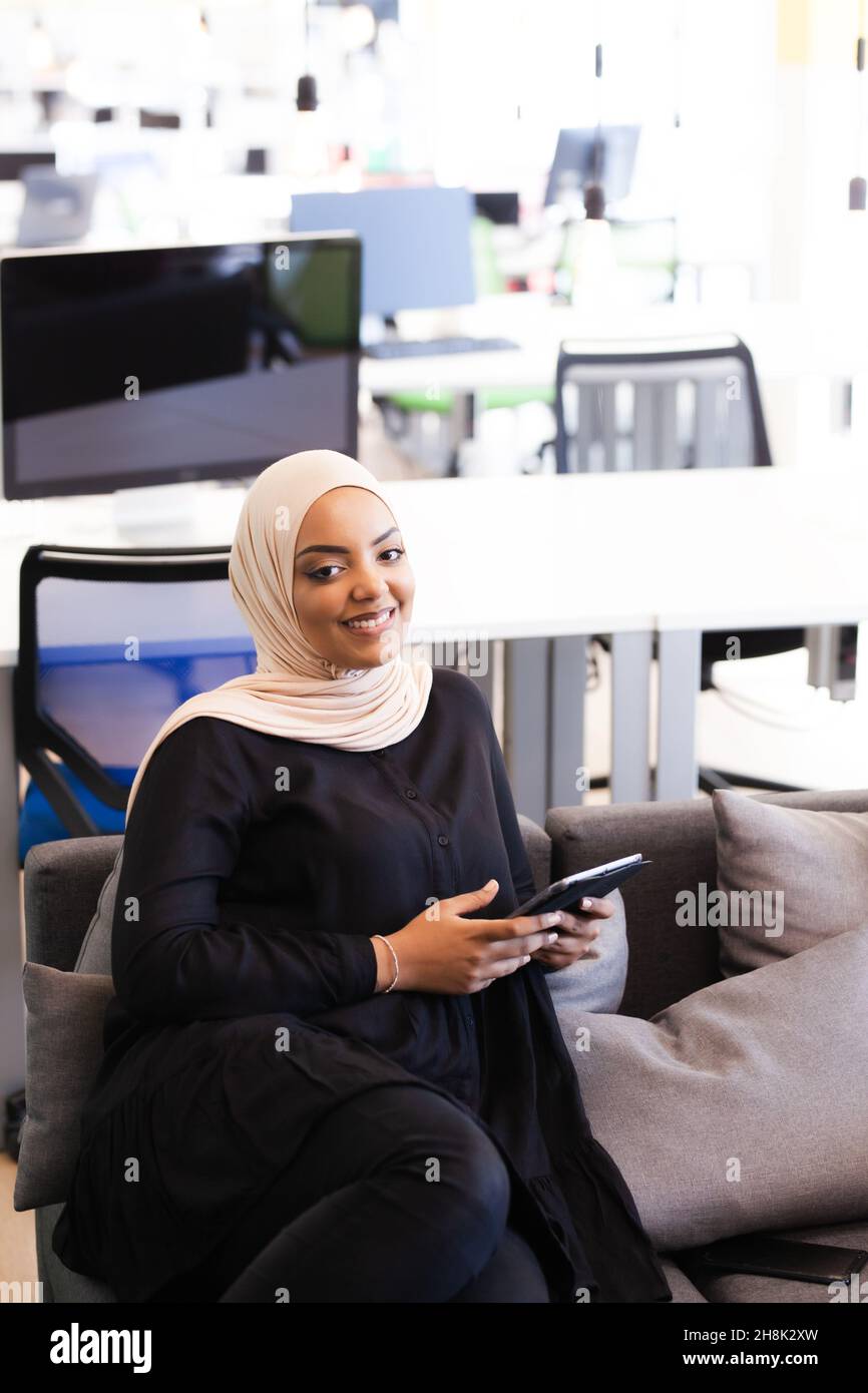 afroamerikanisch-muslimisches Mädchen mit Hijab, das in einem Büro an einem Tablet arbeitet. Stockfoto