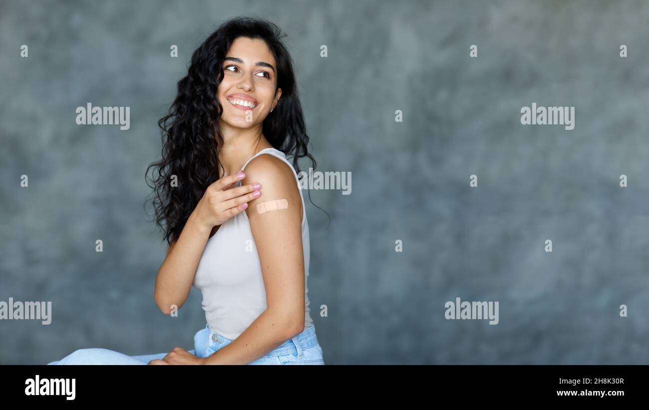 Coronavirus-Impfung. Junge Brünette weiblich, die eine klebende Bandage auf ihrem Arm zeigt und auf den leeren Raum schaut Stockfoto