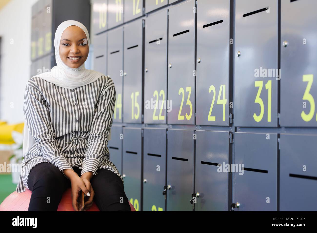 afroamerikanisch-muslimisches Mädchen mit Hijab, das in einem modernen Büro auf dem Gleichgewichtssitz sitzt. Stockfoto