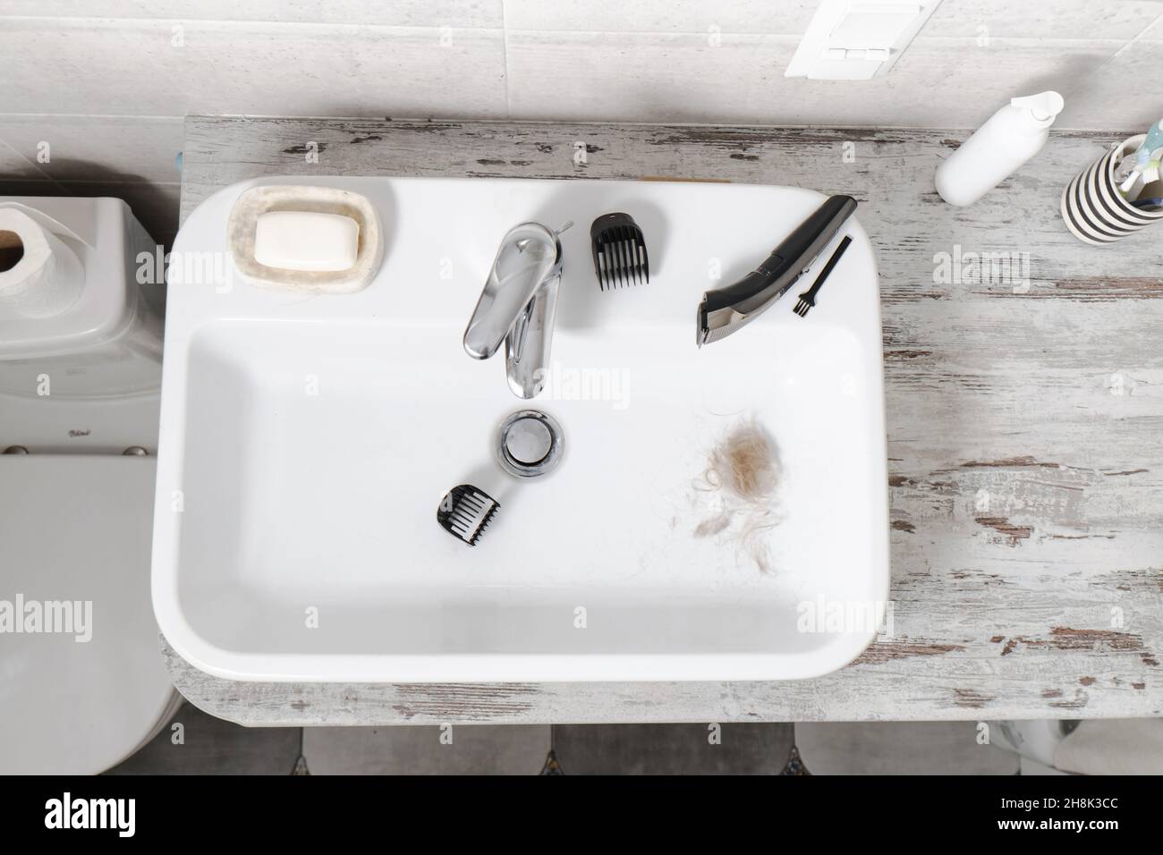 Reinigung elektronischer Rasiermesser im Waschbecken, männliche Selbstpflege und persönliche Hygiene Draufsicht. Haare im Waschbecken. Lange blonde Haare, Maschine Stockfoto