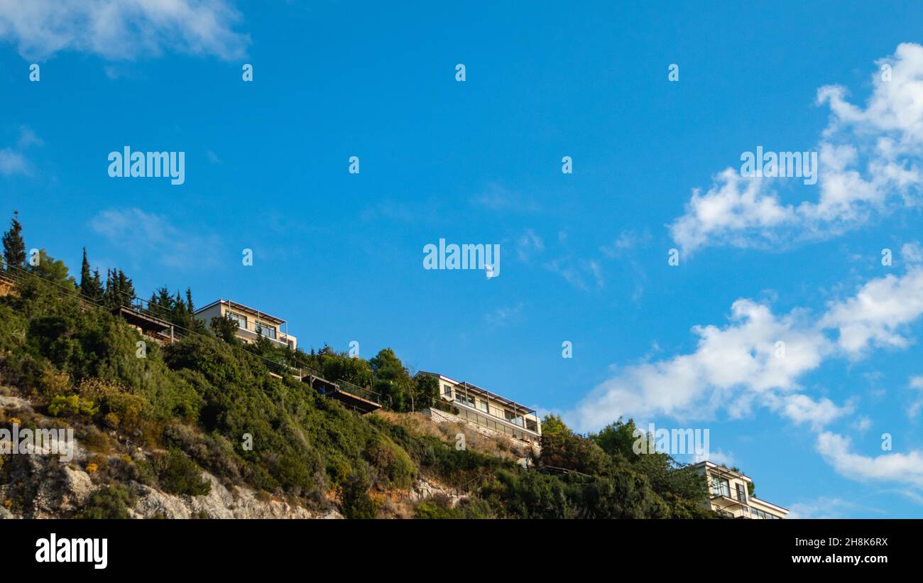 Malerische, lebendige Landschaft mit griechischen Villen auf grünen hohen Hügeln am blauen, malerischen Himmel mit wunderschönen Wolken und jungem Mond auf Lefkada isl Stockfoto