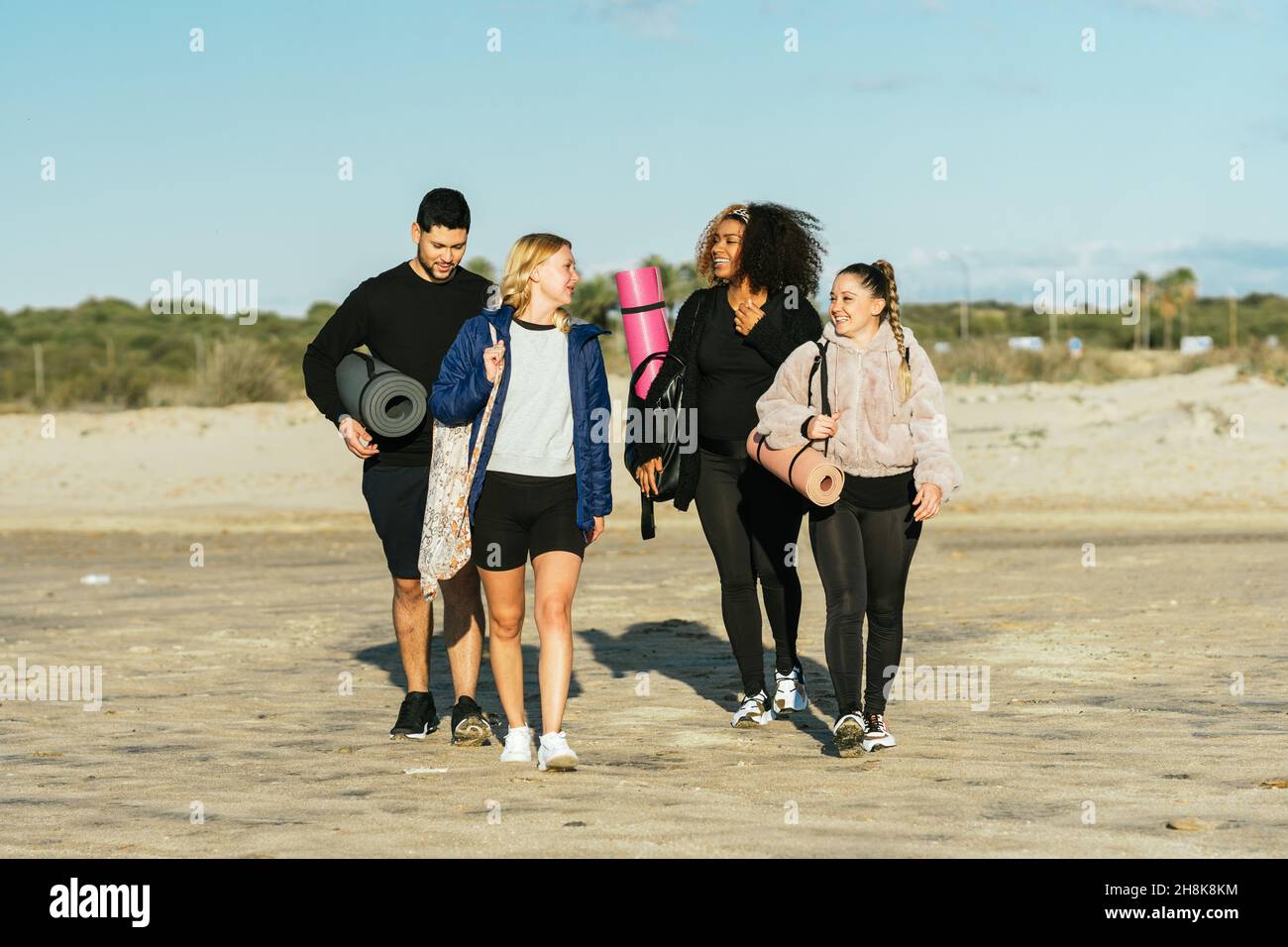 Multiethnische Gruppe läuft am Strand mit Yogamatten und Taschen Stockfoto