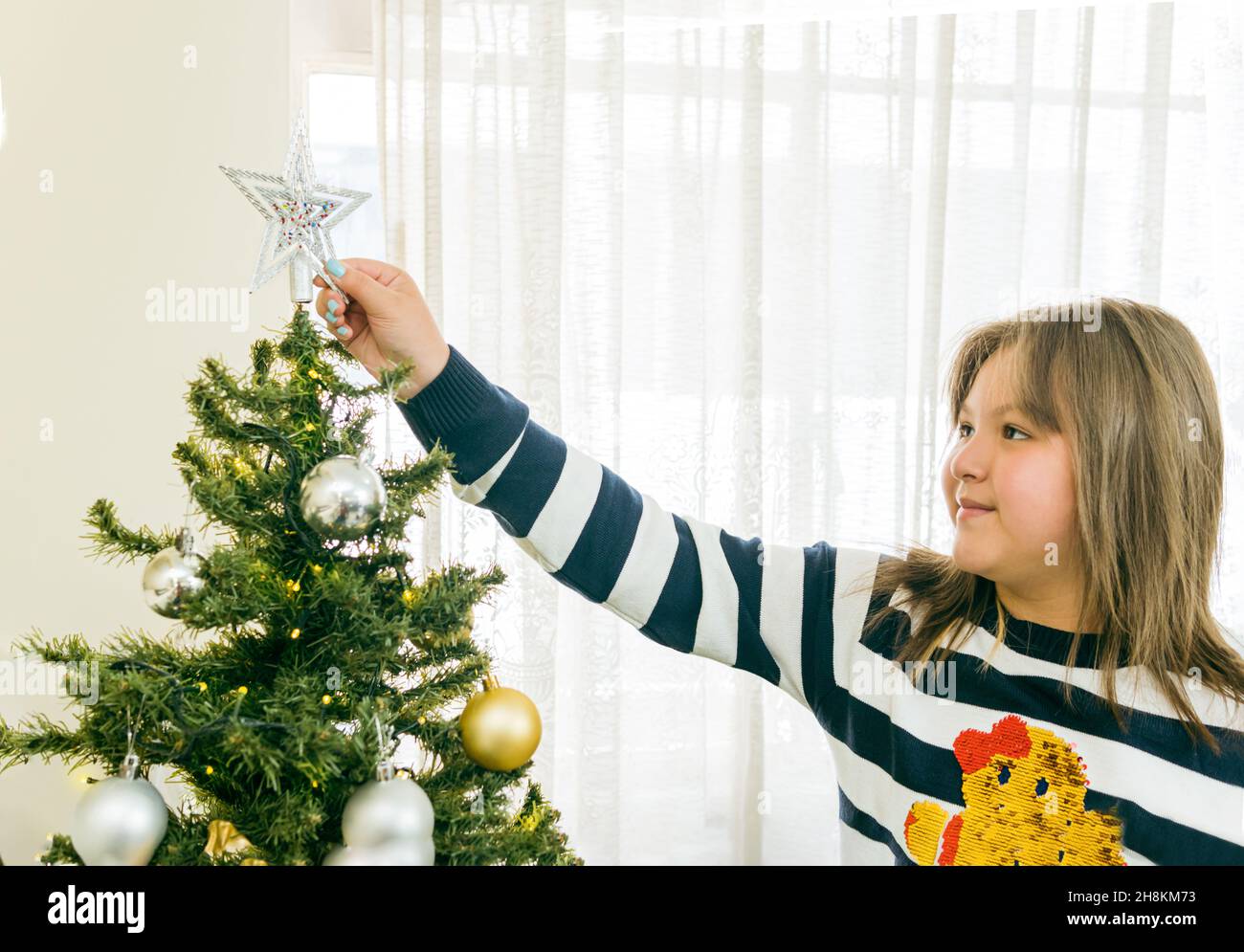 Hispanisch blonde Mädchen setzen Stern auf weihnachtsbaum Stockfoto