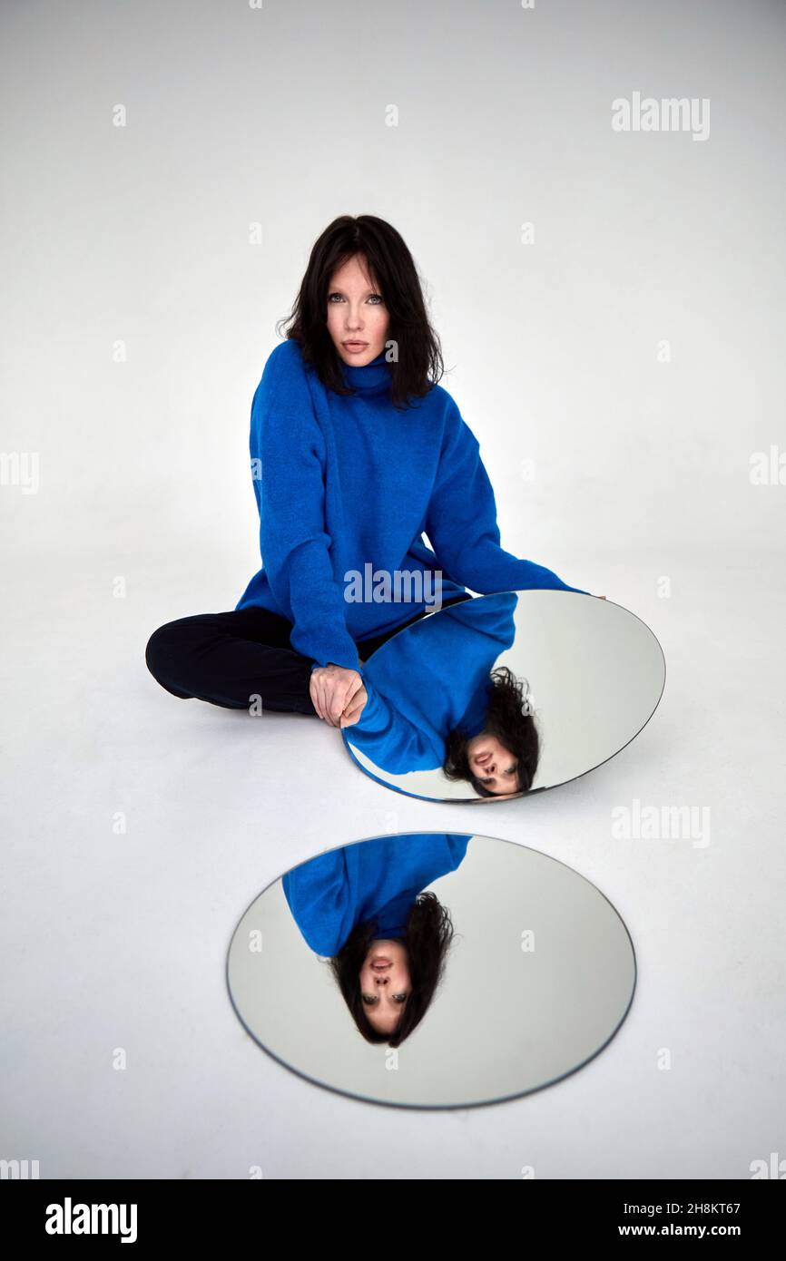Unemotionale Frau, die im Studio mit runden Spiegeln auf dem Boden sitzt und selbstbewusst auf die Kamera blickt Stockfoto