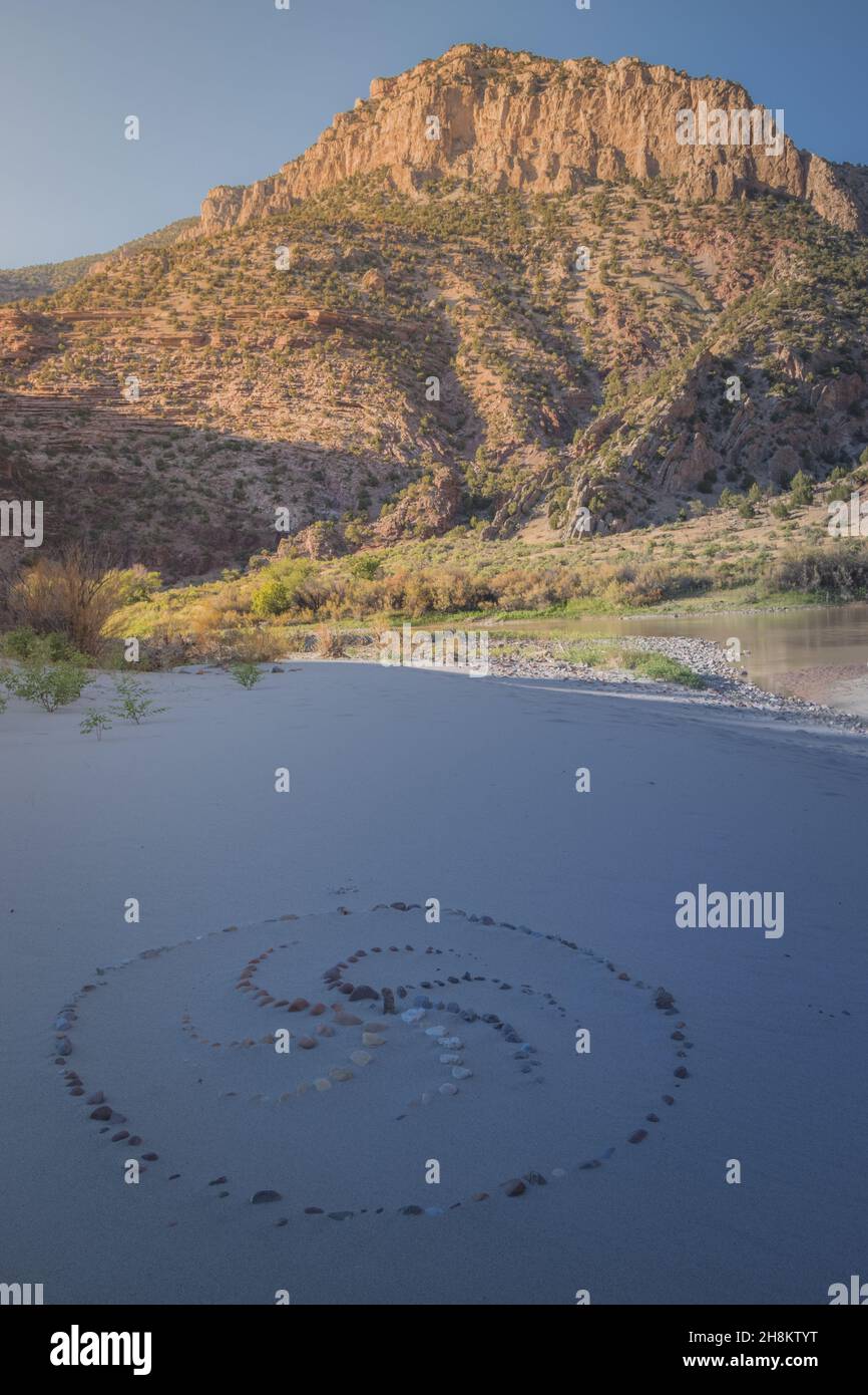 Spiralförmige Ornamente, die mit Steinen auf dem Sand im Echo Park Campground, Dinosaur Nation Monument, Utah und Colorado, USA, gesäumt sind Stockfoto