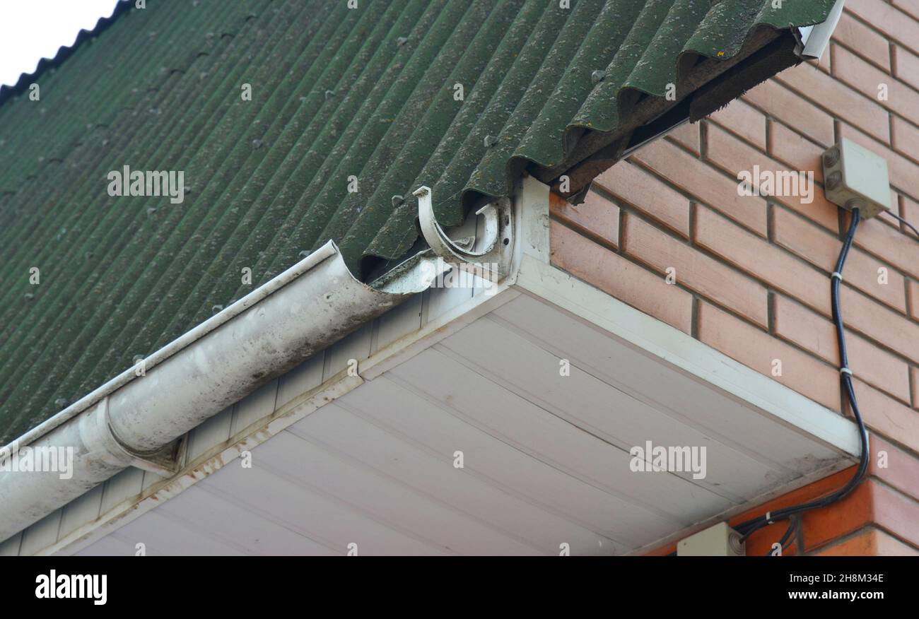 Eine Nahaufnahme eines Dachs mit einer kaputten Dachrinne und einer Öffnung  für Wasserlecks. Eine beschädigte Regenrinne mit einem fehlenden  Dachrinnenrohr auf dem Dachkorn Stockfotografie - Alamy