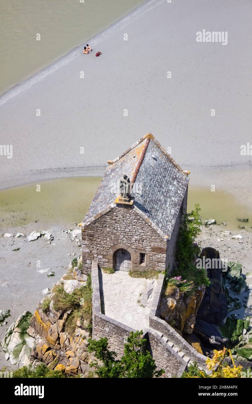 Draufsicht auf die Kapelle am Mont Saint michel, Normandie, Frankreich. Zwei Touristen ziehen es vor, sich am Strand zu bräunen, anstatt den Platz zu besuchen. Stockfoto