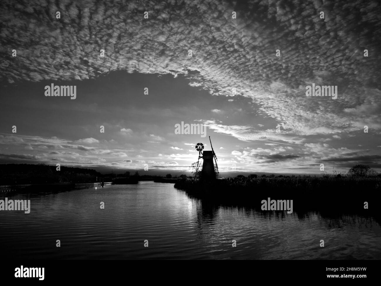 Ein monochromes Bild des Flusses Ant auf den Norfolk Broads mit ikonischer Windmühle und detailliertem Himmel bei einem Herbstuntergang in Ludham, Norfolk, England, Großbritannien. Stockfoto