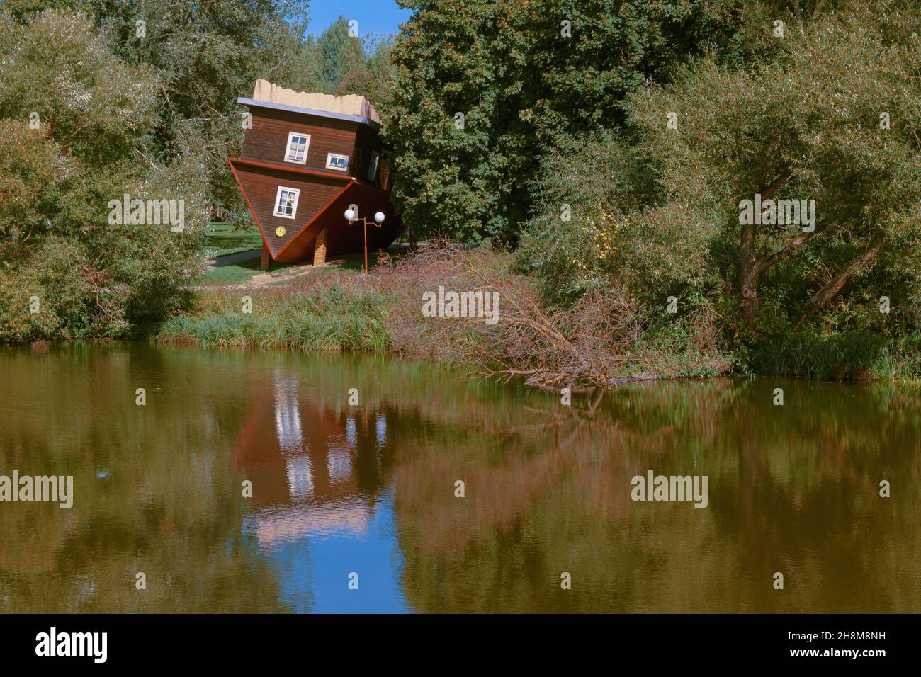 Malerischer Blick auf die Fee. Ein auf den Kopf gedrehtes Haus, ein umgestürzter Baum und ihre Spiegelungen in der Wasseroberfläche des Flusses. Stockfoto