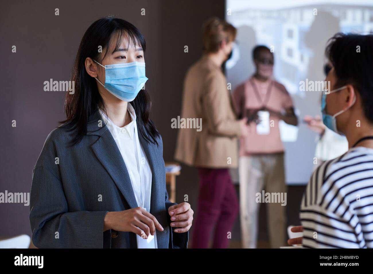 Zwei Geschäftsfrauen in Schutzmasken unterhalten sich während des Geschäftsseminars miteinander Stockfoto