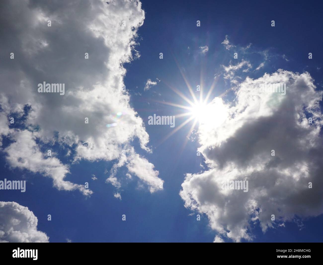 Blauer Sommerhimmel mit Sonnenstrahlen und Wolken Stockfoto