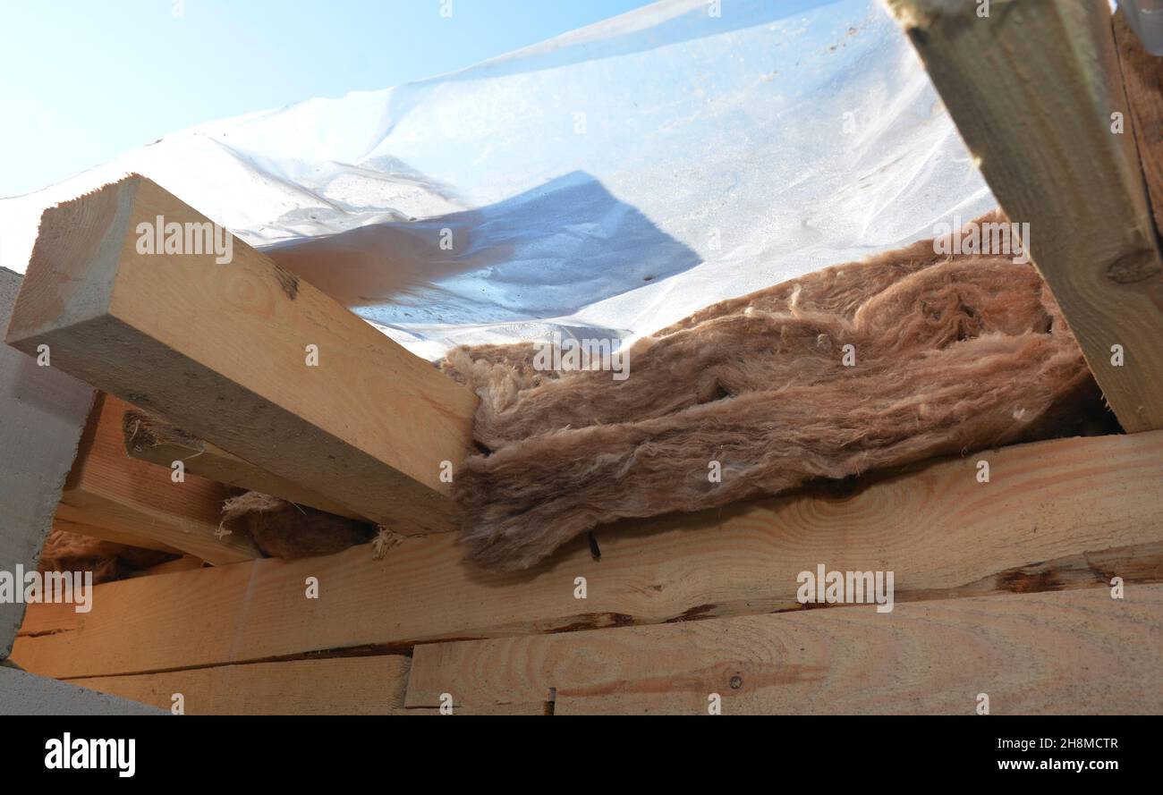Dachkonstruktion und Isolierung. Abdeckung unfertiger Dachkonstruktion mit Mineralwolle mit Polyethylen, Kunststofffolie isoliert. Stockfoto