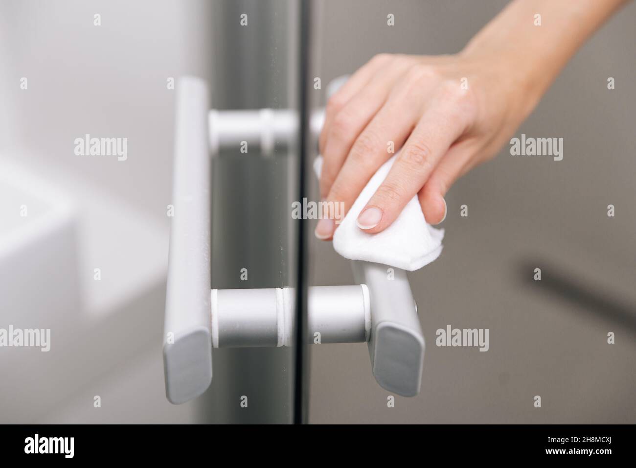 Reinigen Sie die Griffe der Glastür mit einem antiseptischen, feuchten Tuch. Desinfizieren Sie Oberflächen Prävention in Krankenhäusern und öffentlichen Räumen gegen Corona-Virus. Frauenhand Stockfoto