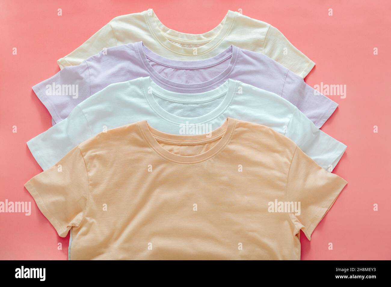 Mehrfarbige T-Shirts Pastellfarben Beige Weiß Lila.T-Shirts Mockup für Design auf Farbe Koralle rosa Hintergrund. Gestapelte Basic T-Shirts Stockfoto