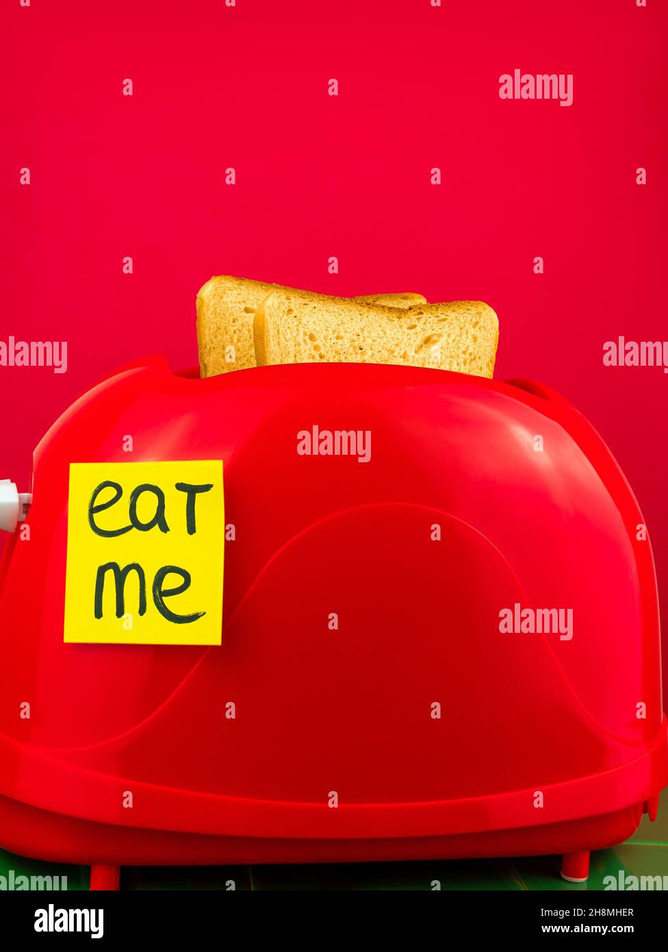 Roter Toaster mit knusprigen, frischen Brotscheiben in der Küche mit grünen Kacheln. Morgen Toast Frühstück Idee kreativen Minimalismus Konzept. Eat me gelbe Aufkleber min Stockfoto