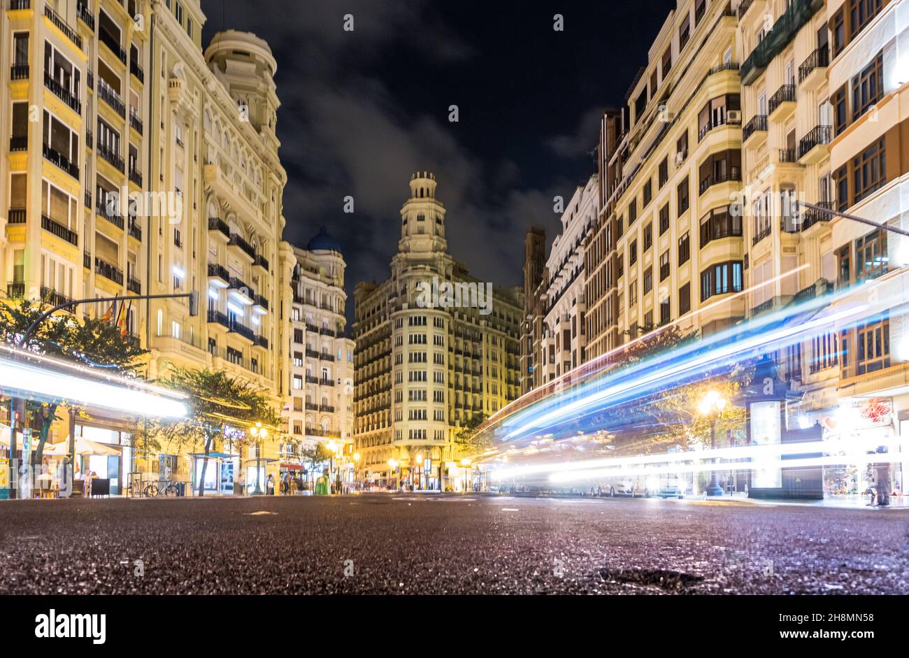 Langaufnahme der Lichtspuren von Fahrzeugen auf dem Hauptplatz von Valencia vom Asphalt aus, der seine Architektur zeigt Stockfoto