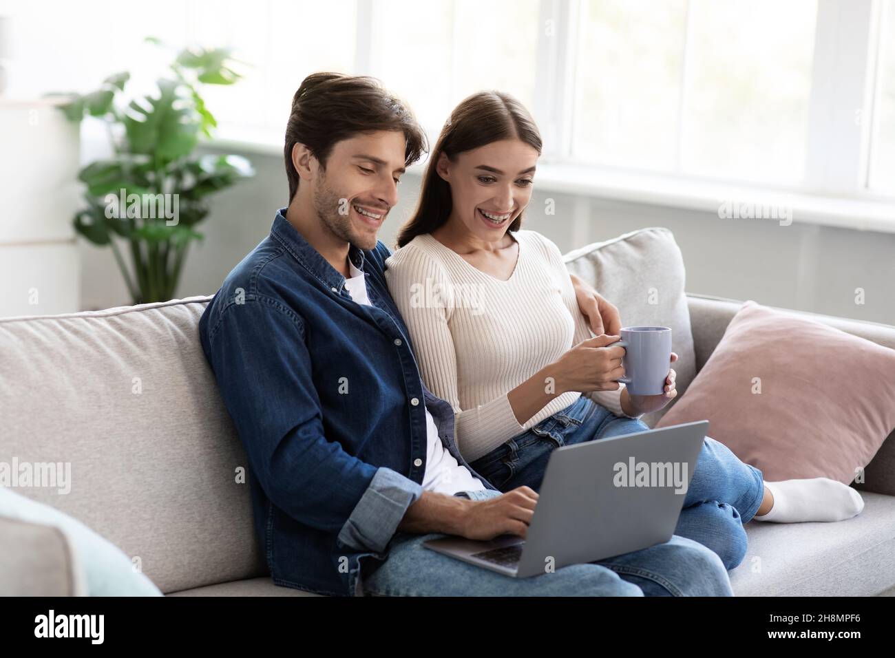 Fröhlicher, tausendjähriger europäischer Ehemann und Ehefrau verbringen Freizeit und Wochenende zusammen und schauen sich einen Laptop an Stockfoto