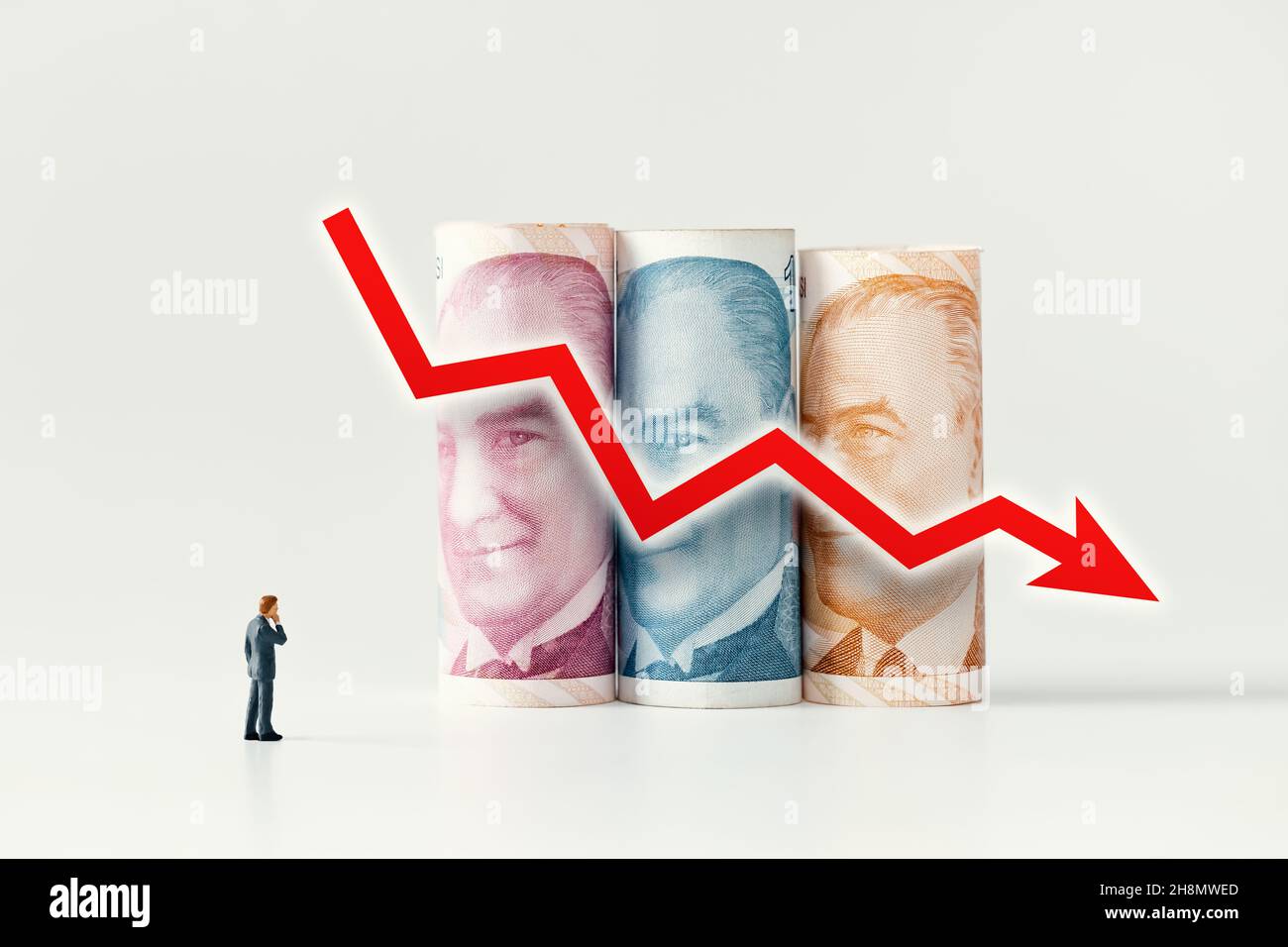 Businessman Figur, die über türkisches Geld (Lira) nachdenkt und sich diese anschaut, rollt Banknoten und roter Pfeil geht auf weißem Hintergrund nach unten. Abwertung Stockfoto