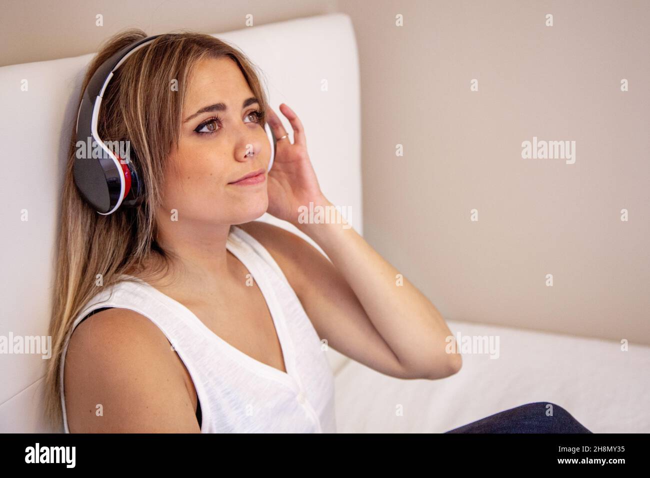 Frau, die Musik hört, sitzt mit Kopfhörern auf dem Bett in ihrem Zimmer. Mädchen mit geschlossenen Augen. Genießen Sie die Musik. Stockfoto