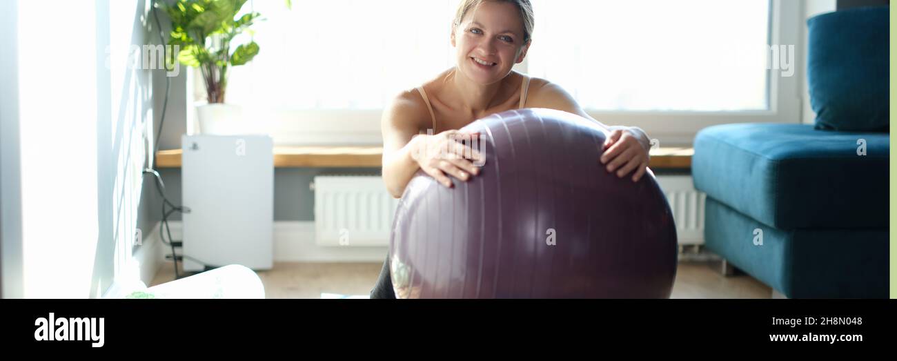 Porträt einer glücklichen jungen Frau mit großem Gymnastikball auf dem Teppich zu Hause Stockfoto
