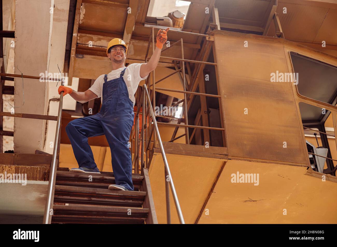 Fröhlicher Arbeiter, der im Technikgeschäft auf der Treppe steht Stockfoto