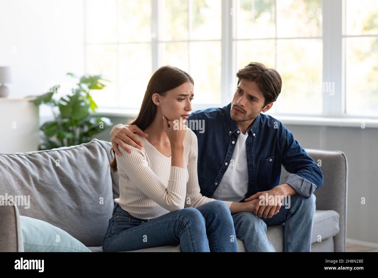 Serious vorsichtig jungen europäischen Kerl beruhigt verärgert unglückliche Dame im Wohnzimmer Interieur Stockfoto