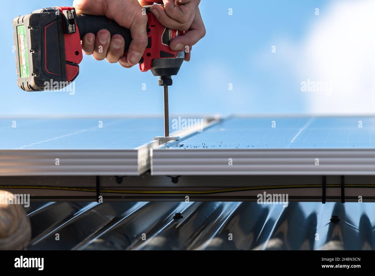 Nicht identifizierter Mann, der Solarmodul mit dem Schraubendreher am Dachträger befestigt Stockfoto