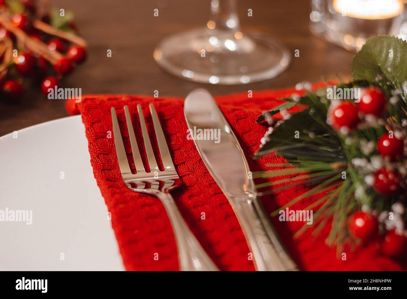 Weihnachtliche Tischeinstellung. Teller und Besteck auf Serviette. Vorbereitung auf das festliche Abendessen. Kerzen brennen am Heiligabend auf dem Tisch. Stockfoto