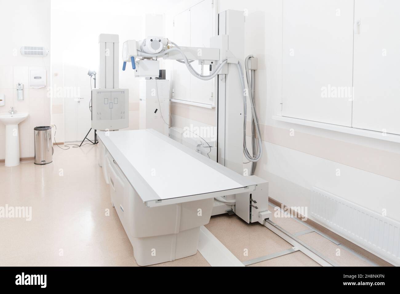 Röntgenabteilung im modernen Krankenhaus. Röntgenraum mit Scangerät und leerem Bett. Techniker, der ein Röntgengerät anpasst. Scannen von Brust, Herz Stockfoto