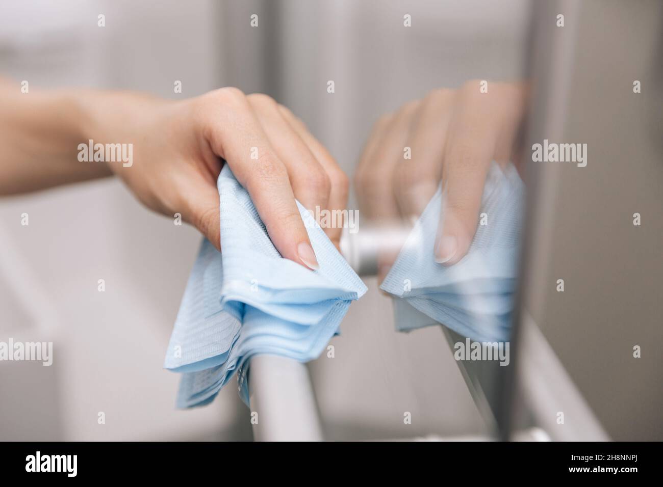 Reinigen Sie die Griffe der Glastür mit einem antiseptischen, feuchten Tuch. Frau Hand mit Handtuch für die Reinigung Zimmer Tür Link. Desinfizieren von Oberflächen in Stockfoto