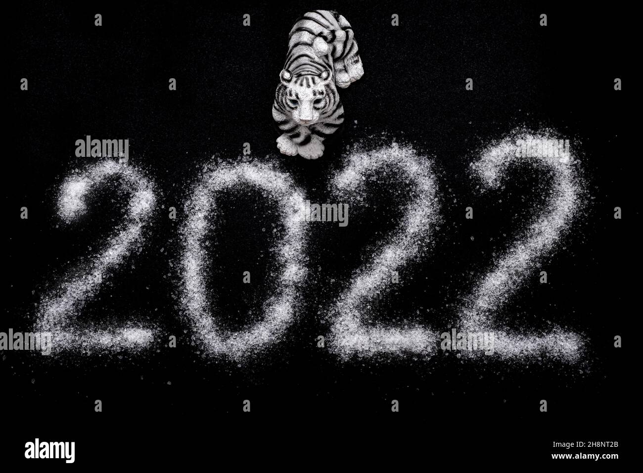 Frohes Neues Jahr 2022. Chinesisches Neujahr 2022. Toy Tiger und das Datum 2022 ist mit Salz wie Schnee geschrieben, isoliert auf schwarzem Hintergrund, Draufsicht. Stockfoto