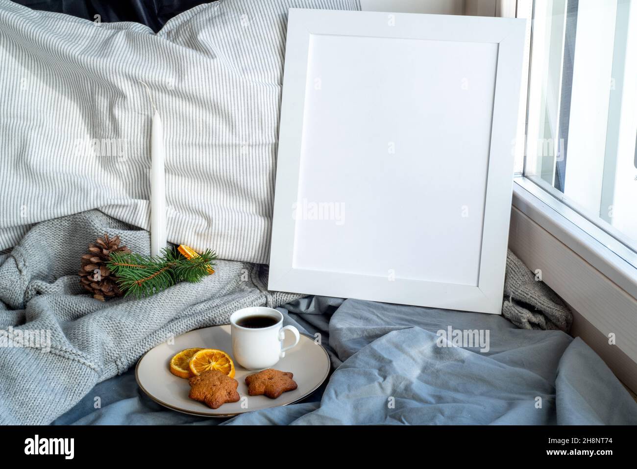 Gemütliches Weihnachtsfrühstück Stillleben Szene in der Nähe des Fensters. Winterausstattung. Weißer Bilderrahmen-Mockup.Tasse Kaffee mit Vollkornplätzchen, pil Stockfoto