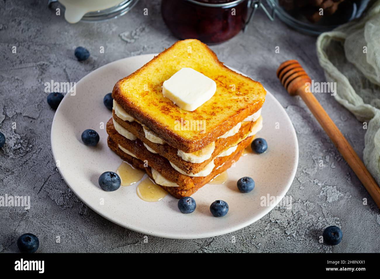 French Toast mit Banane, Heidelbeere, Honig und Erdbeermarmelade. Köstliches Frühstück oder Brunch mit Toast und Keksen Stockfoto