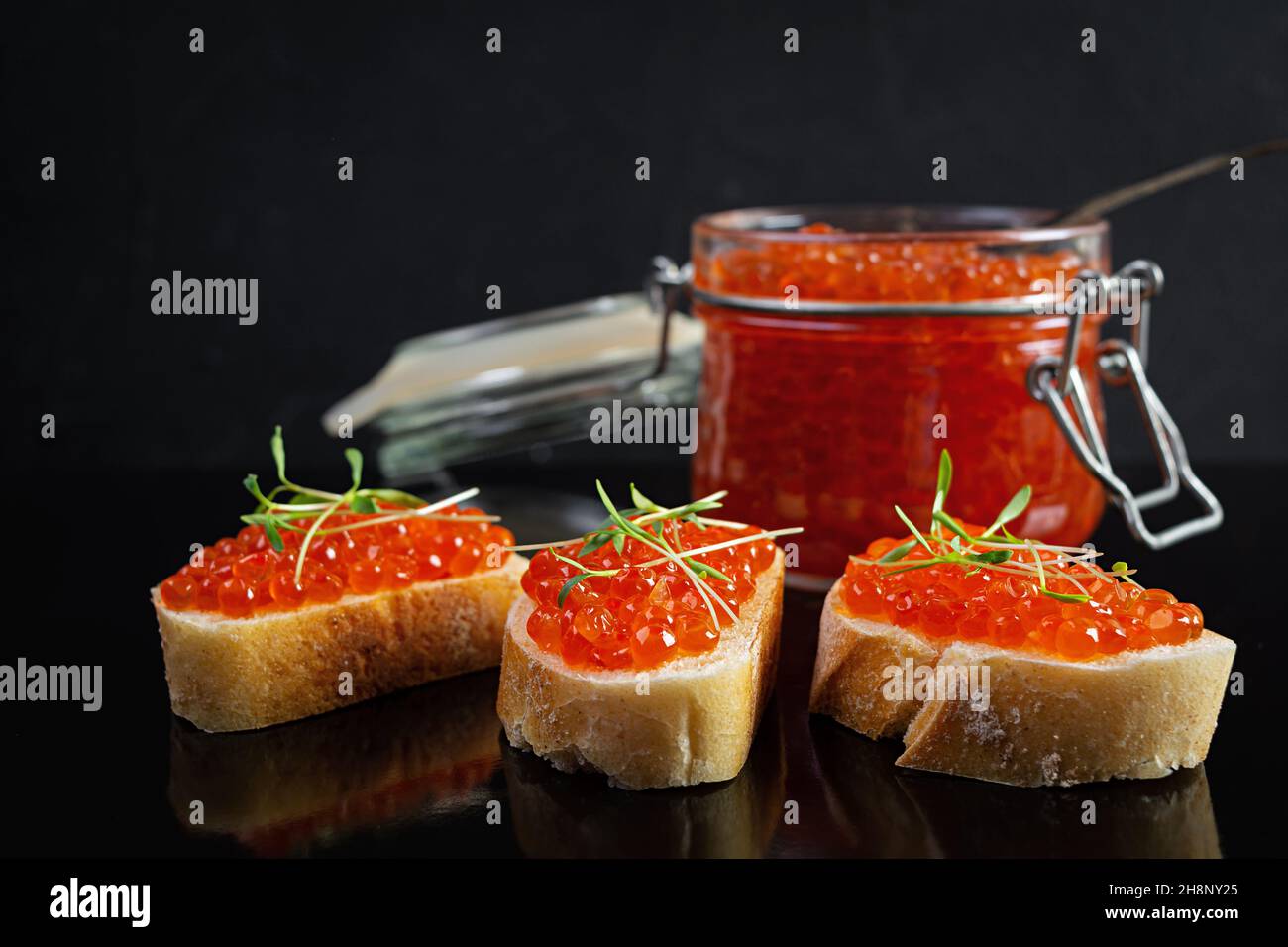 Köstlicher frischer roter Kaviar mit Baguette-Toasts auf dunklem Hintergrund Stockfoto