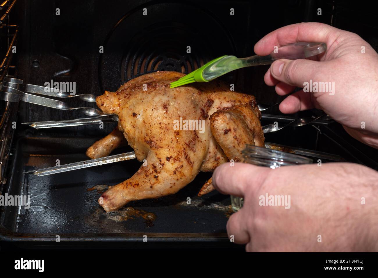 Männliche Hände decken rohes ganzes Huhn, das im Ofen mit Sauce röstet, aus nächster Nähe. Ein Fleischgericht für ein festliches Abendessen vorbereiten. Natürliche hausgemachte gesund Stockfoto