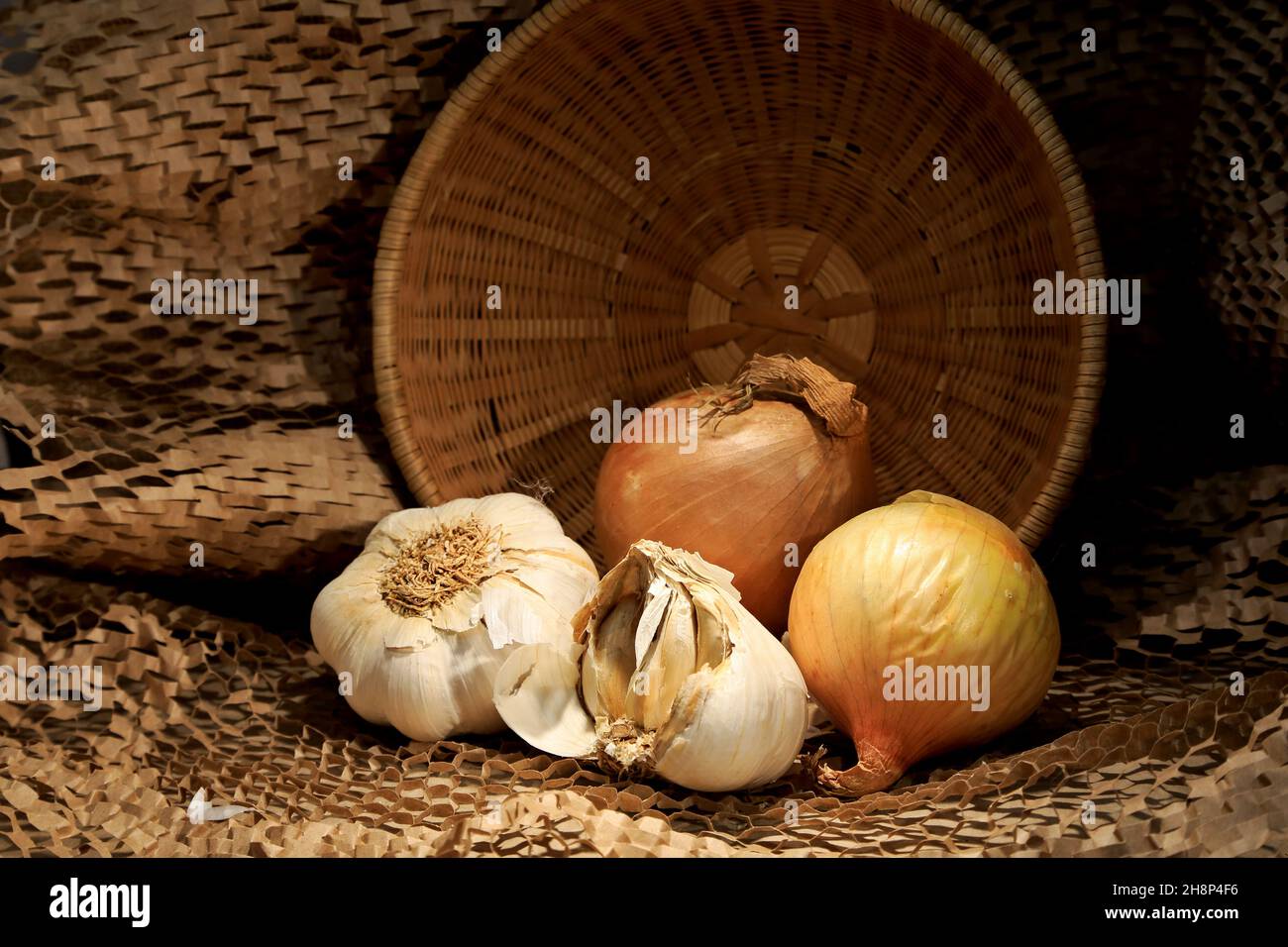 Zwiebel und Knoblauch mit einem braunen Korb auf einem Tisch Stockfoto