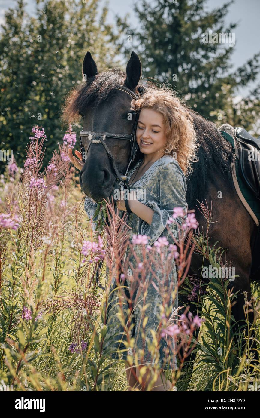 Frau in Wildblumen im Gespräch mit Pferd, vertikale Aufnahme. Stockfoto