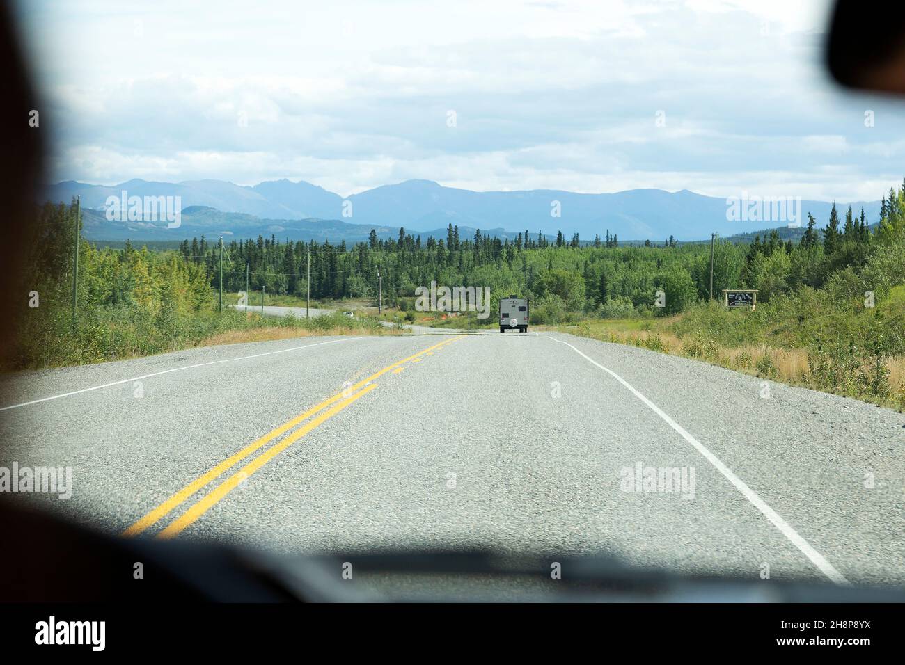 Der Alaska Highway durch die Windschutzscheibe eines Fahrzeugs, das im Yukon, Kanada, fährt. Das Fahrzeug befindet sich auf einer Autoreise. Stockfoto