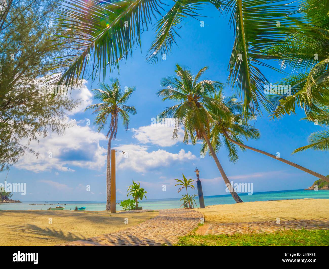 Landschaftsansicht auf leerem Strand mit Dusche mit frischem Wasser vor dem welligen Meer und dramatischen bewölkten Himmel bei Sonnenaufgang mit Palmen. Kleiner Pfad Stockfoto